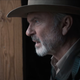 A bearded, hat-and-uniform-clad Sam Neill looks out a window in alien drama Invasion.